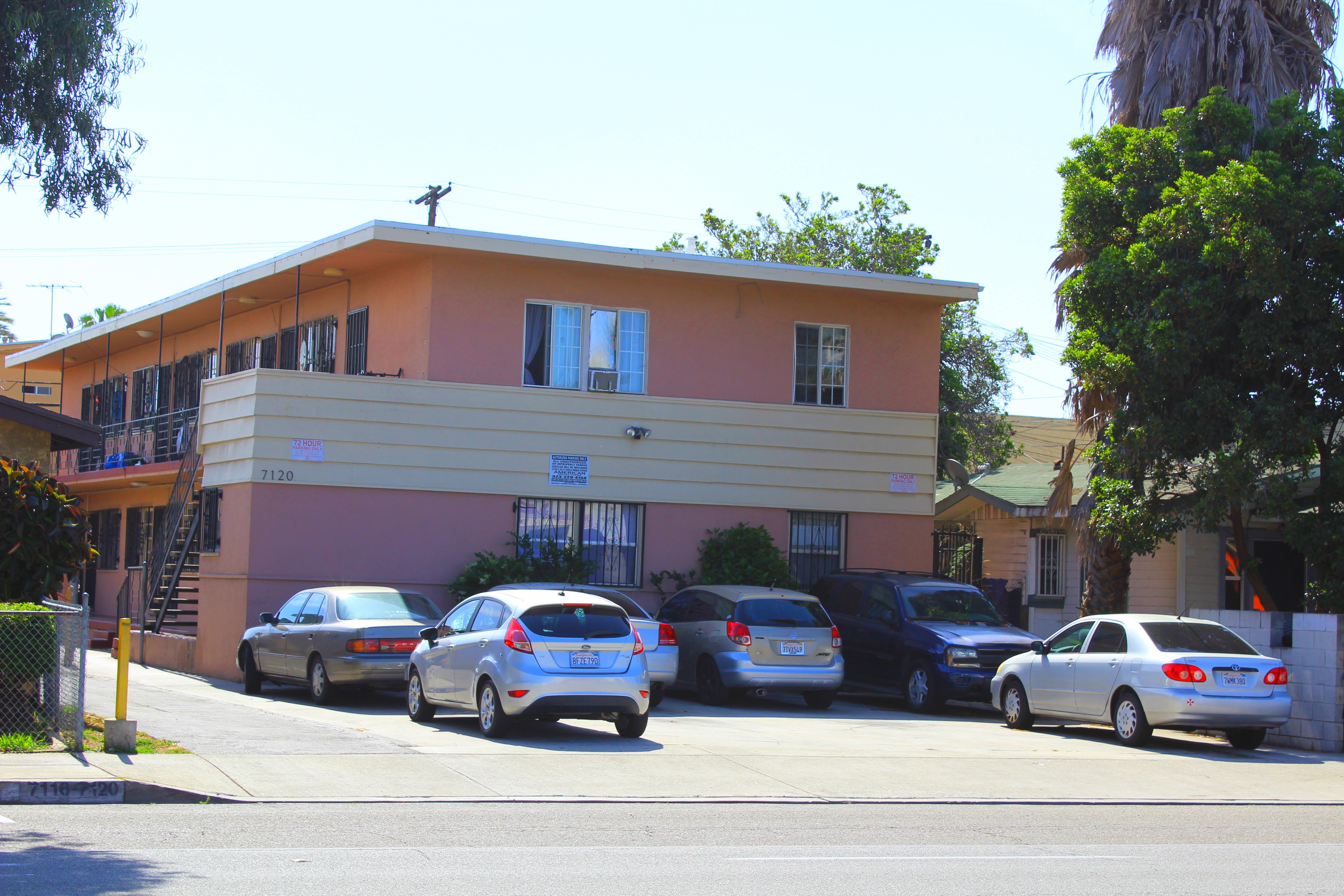 A building with a pink and yellow facade has cars parked in front.